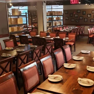 Empty restaurant dining room with set wooden tables and red upholstered chairs.
