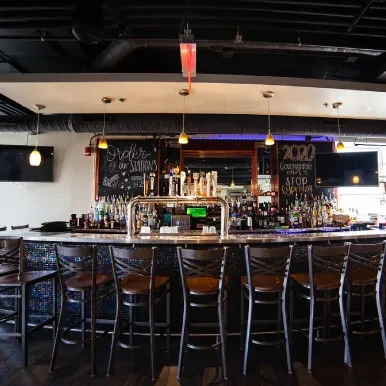 Modern bar counter, stocked bottles, stools, and 'COVID-19' chalkboard.