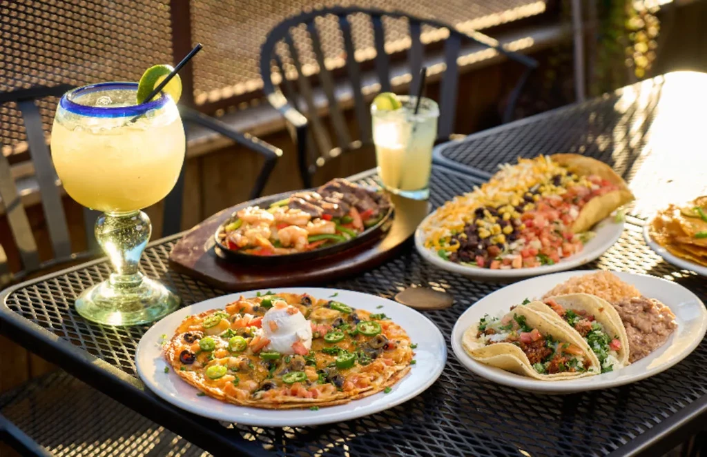 Mexican food and drinks, including fajitas, on a sunny outdoor table.