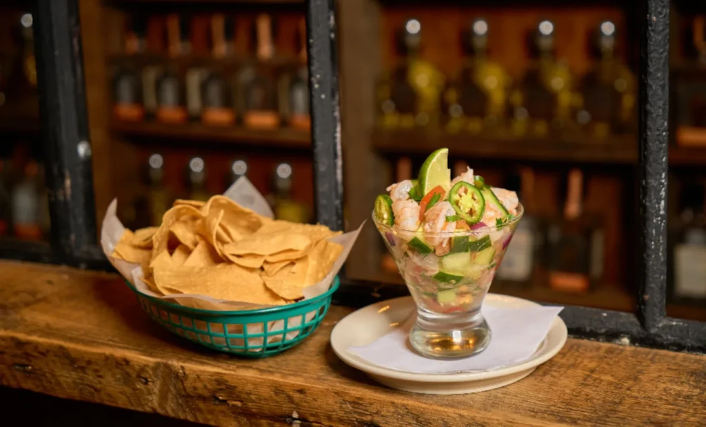 Golden tortilla chips and shrimp ceviche on a rustic bar counter.