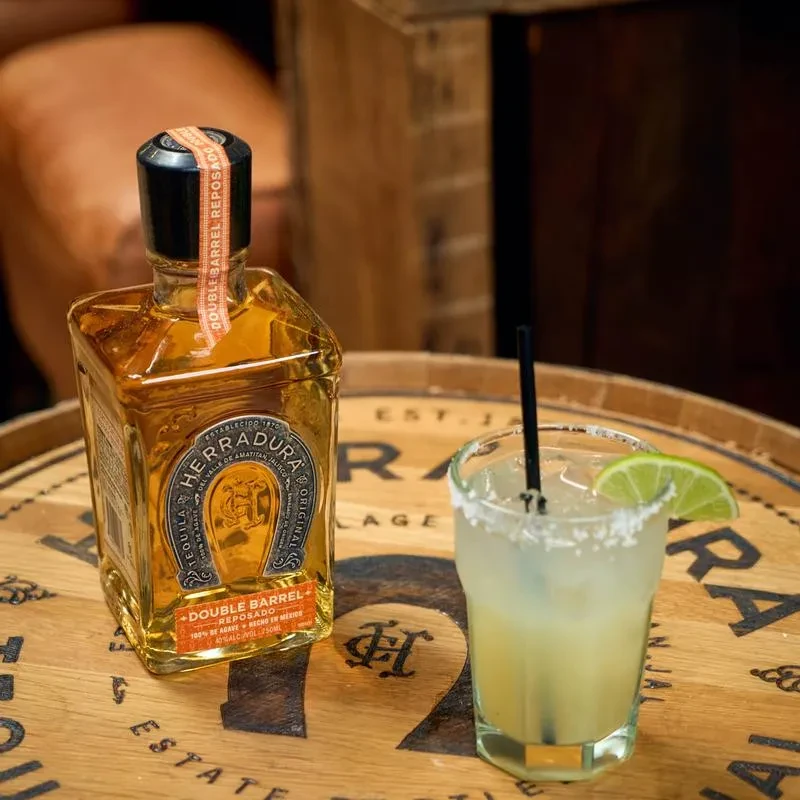 Herradura Double Barrel Reposado tequila and salt-rimmed margarita on wood.