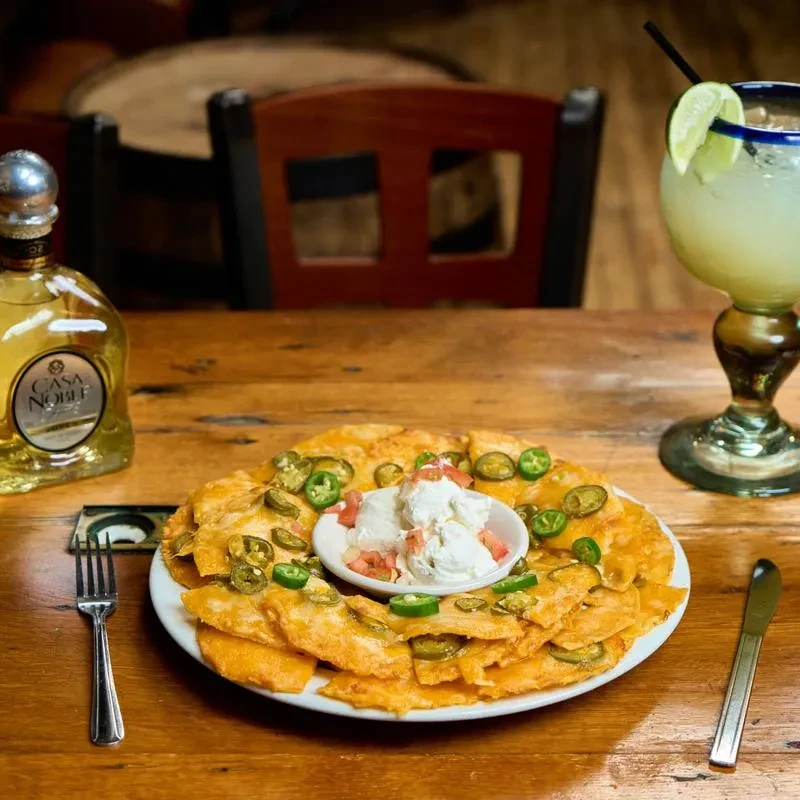Nachos with melted cheese, jalapeños, a tequila bottle, and margarita.