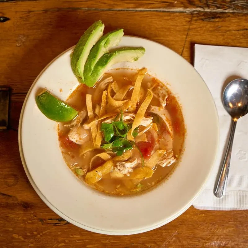 Chicken tortilla soup garnished with avocado, lime, and cilantro.