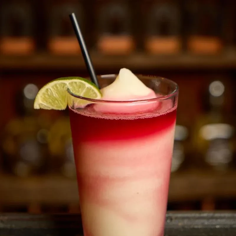 Layered red, pink, and white frozen drink with lime and straw.