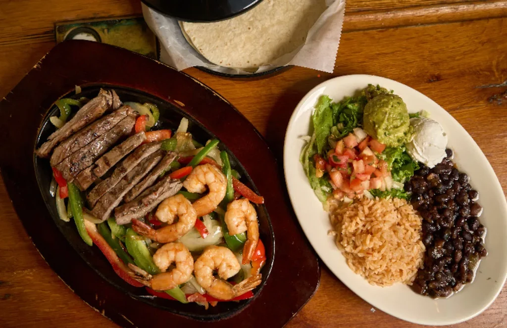 Sizzling fajitas, rice, beans, and tortillas on a rustic wooden table.