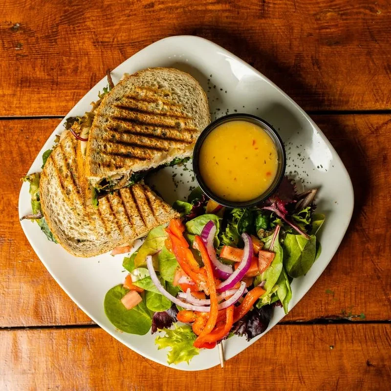 Grilled panini with green filling, side salad, and dressing on wood.