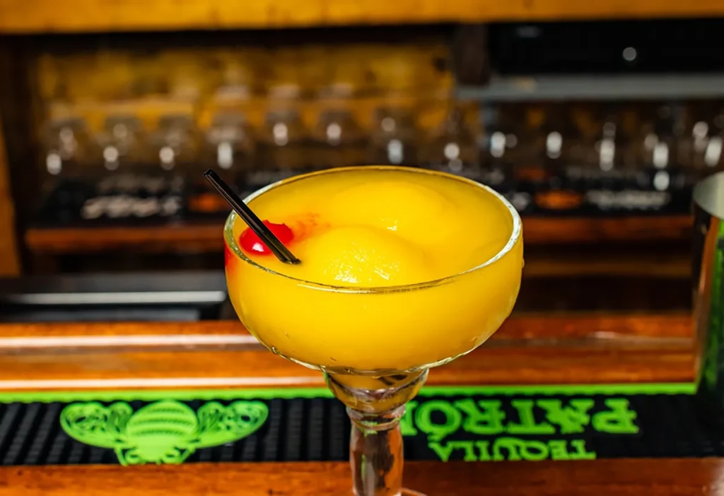 Frozen yellow drink in margarita glass with red fruit, on bar.