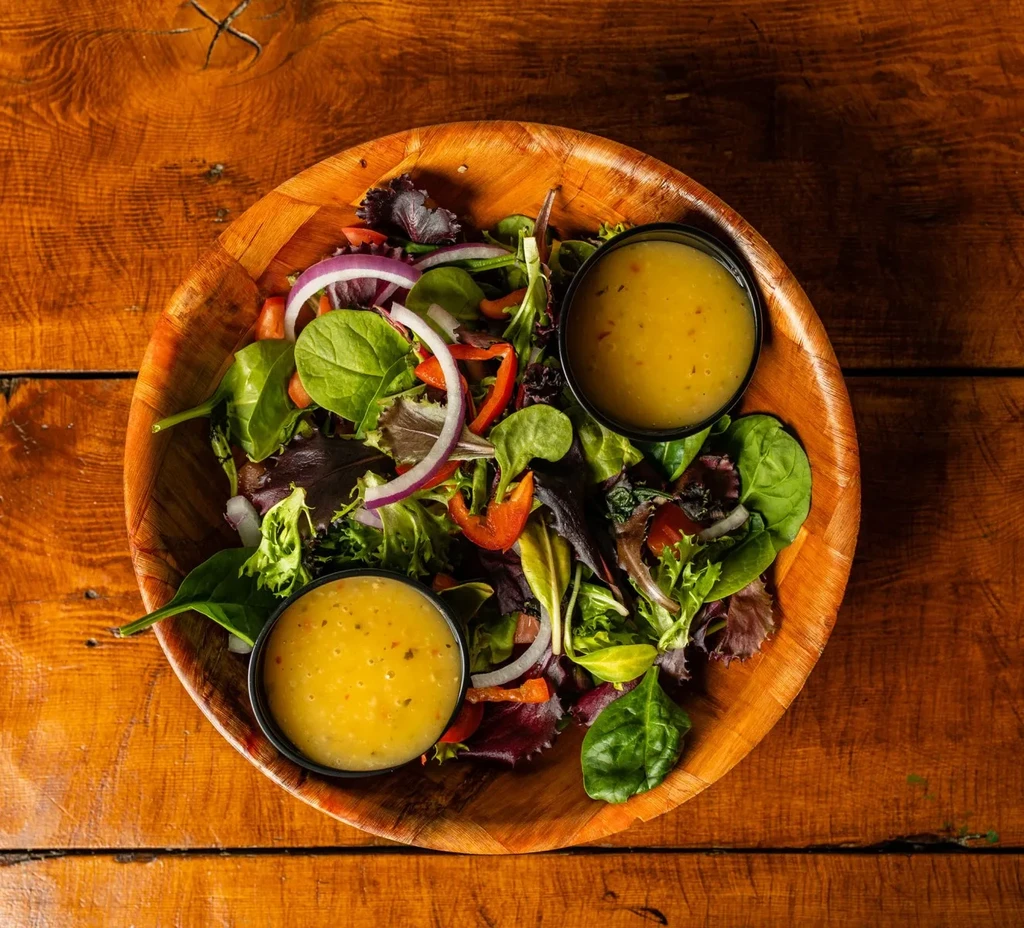 Top-down view of a colorful salad in a wooden bowl with dressing.