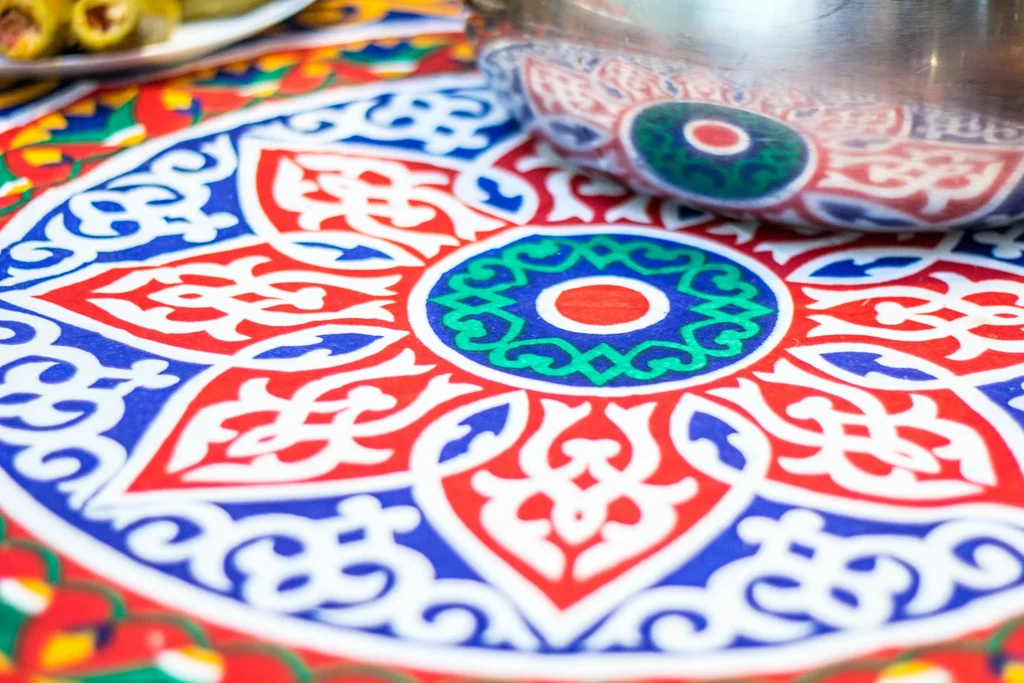 Intricate geometric and floral patterned mat; blurred food background.