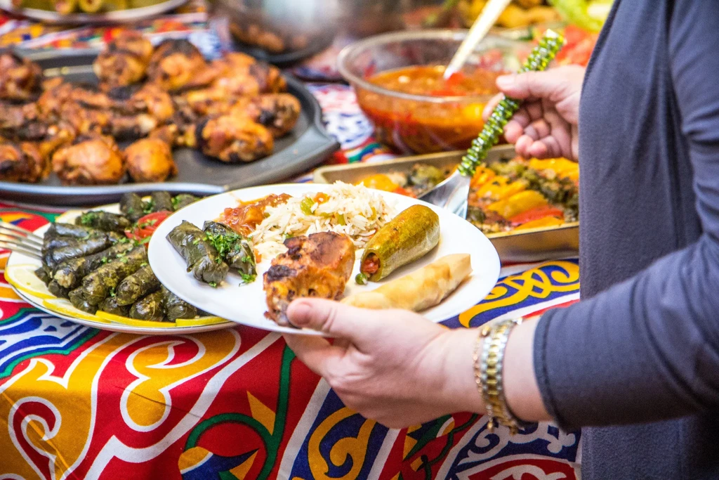 Hand holding a plate of chicken, rice, and stuffed vegetables at a buffet.