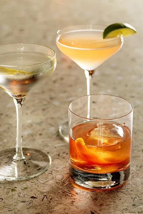 Three distinct cocktails in different glasses with lemon, lime, and orange garnishes.