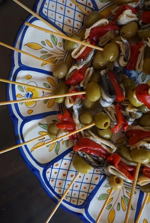 Top-down view of olive, anchovy, pepper skewers on a patterned plate.