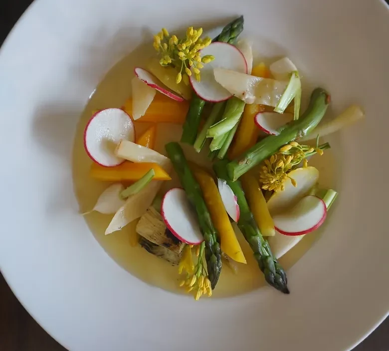 Artfully plated fresh vegetables in a light broth with edible flowers.