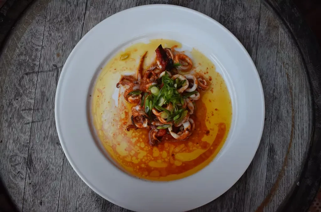 Pan-seared calamari with chili-spiced oil and green onions on wood.