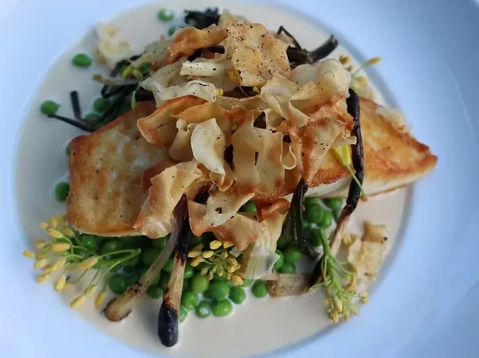 Seared golden protein with crispy shavings, green peas, and creamy sauce.