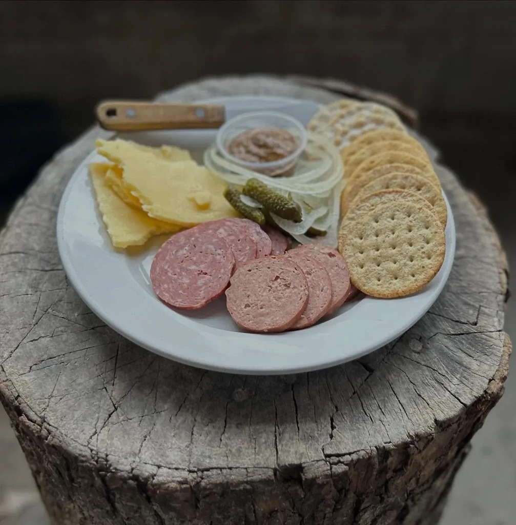 Platter of cheese, meats, pickles, crackers, and mustard on a log.
