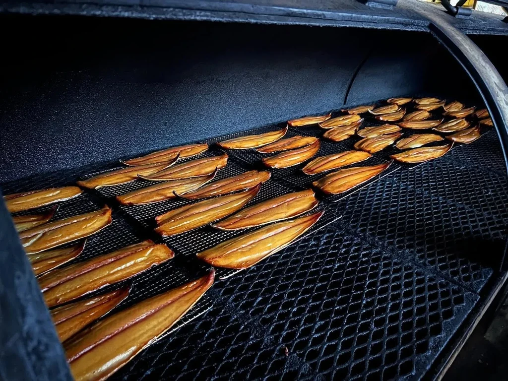 Golden-brown smoked fish fillets neatly arranged on grates in a dark smoker.