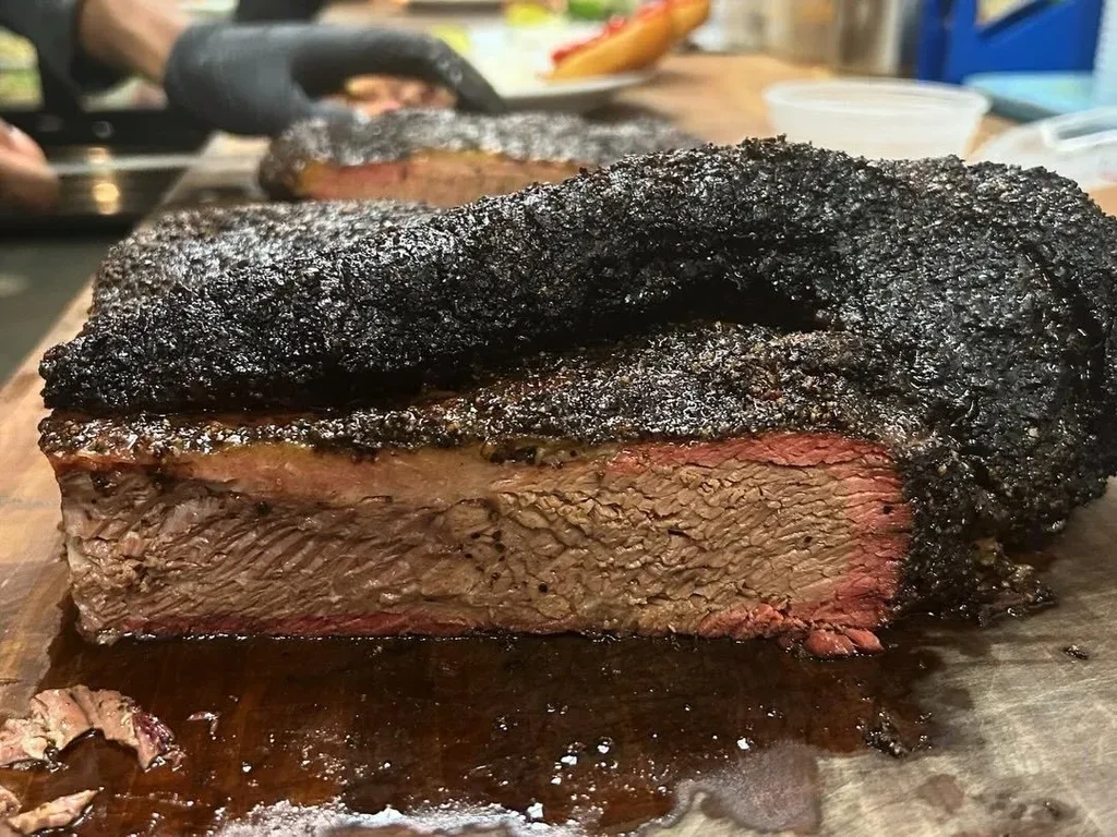 Cut smoked brisket with dark bark, pink smoke ring, on wooden board.