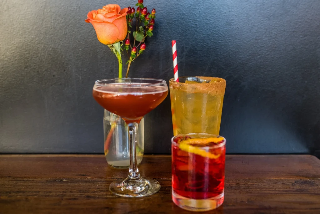 Still life with three cocktails, an orange rose, and red berries.