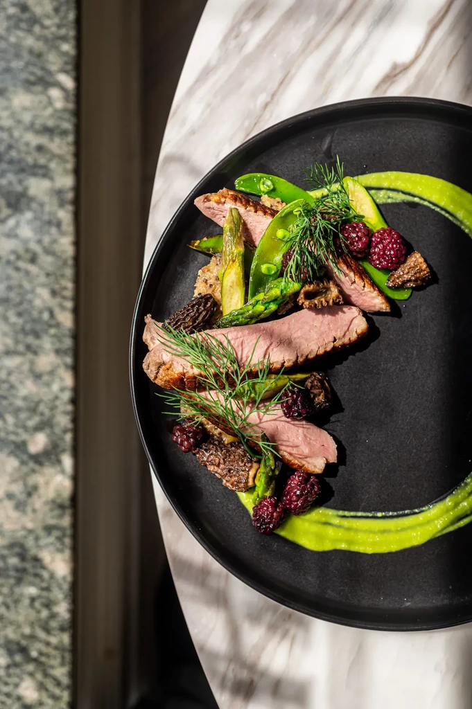 Gourmet dish with seared meat, asparagus, berries, mushrooms, and green sauce.