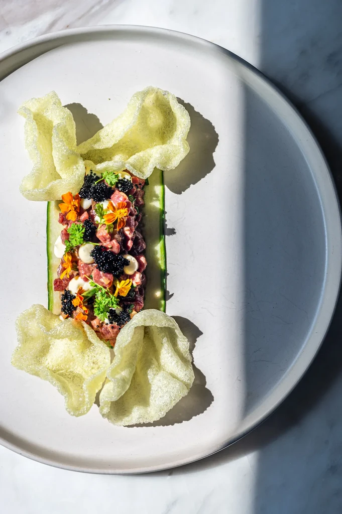 High-end tartare dish with caviar, herbs, edible flowers, cucumber, and crisps.
