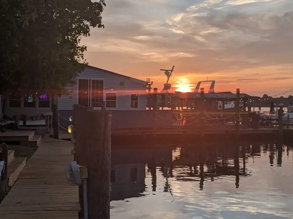 Vibrant sunset behind a waterfront restaurant with a dock and boats.