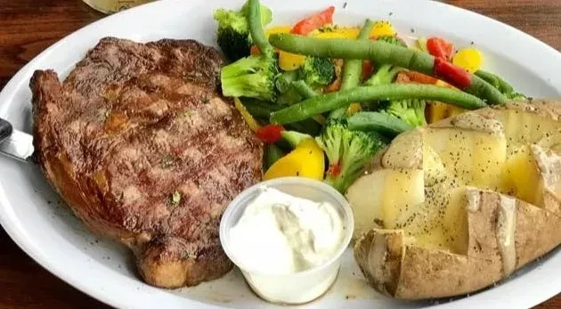 Well-plated meal: grilled steak, vegetables, baked potato, and creamy sauce.