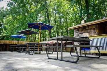 Empty outdoor patio with dark metal tables, umbrellas, and a rustic building.