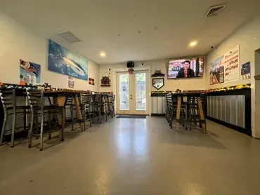 Empty casual restaurant interior with high-top tables, bar, and TV.
