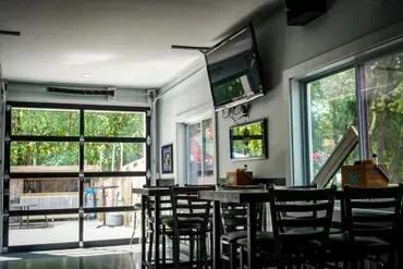 Modern restaurant interior: high-top tables, open glass wall to patio.
