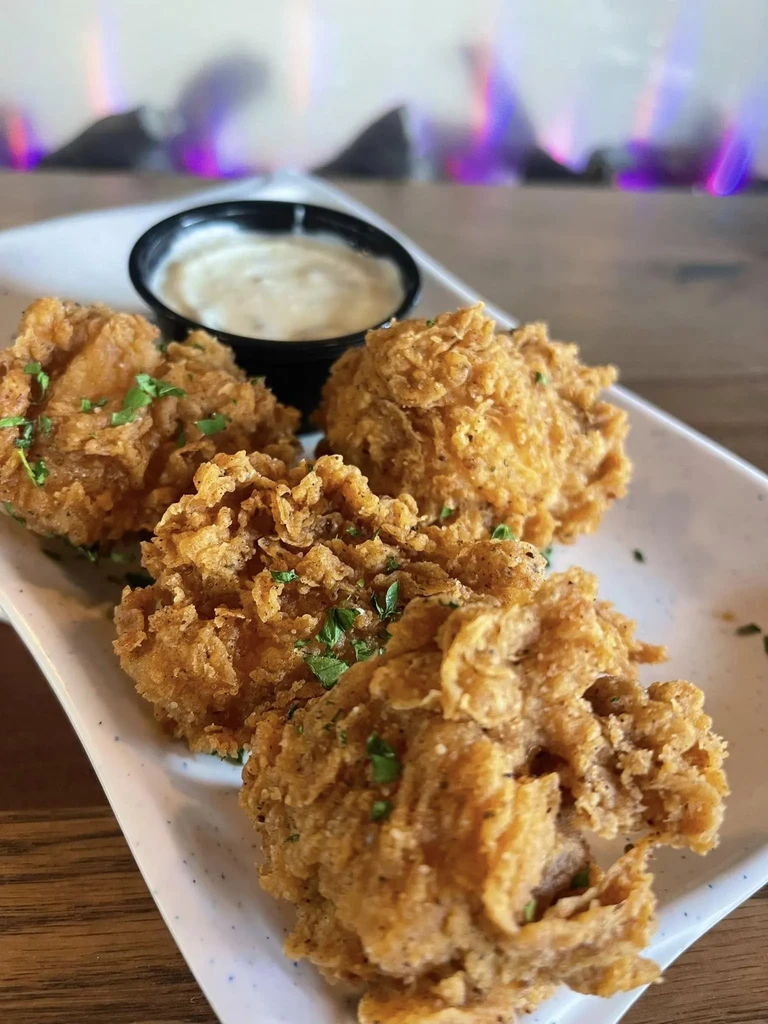 Four golden-brown fried food with herbs, sauce, and purple flames.