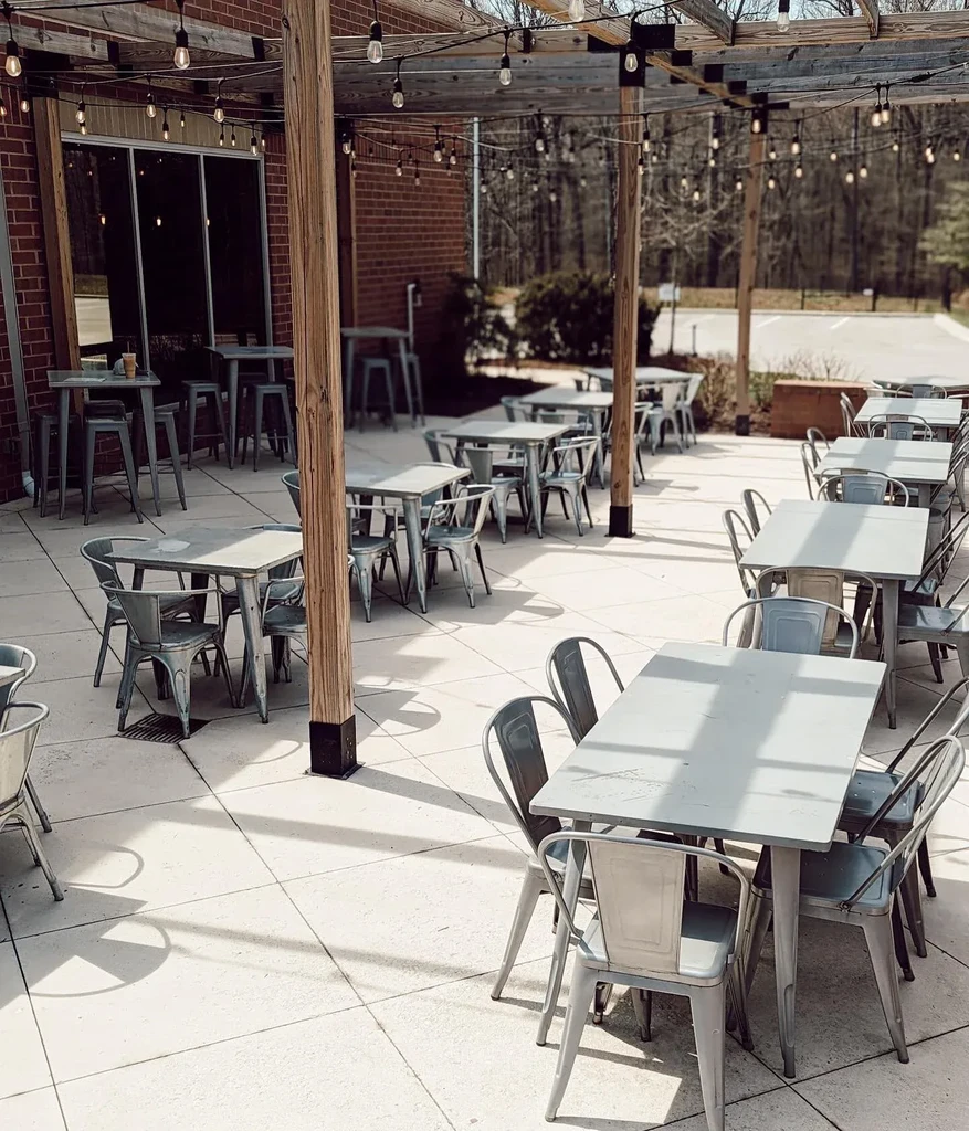 Empty restaurant patio with gray tables, pergola, and string lights.