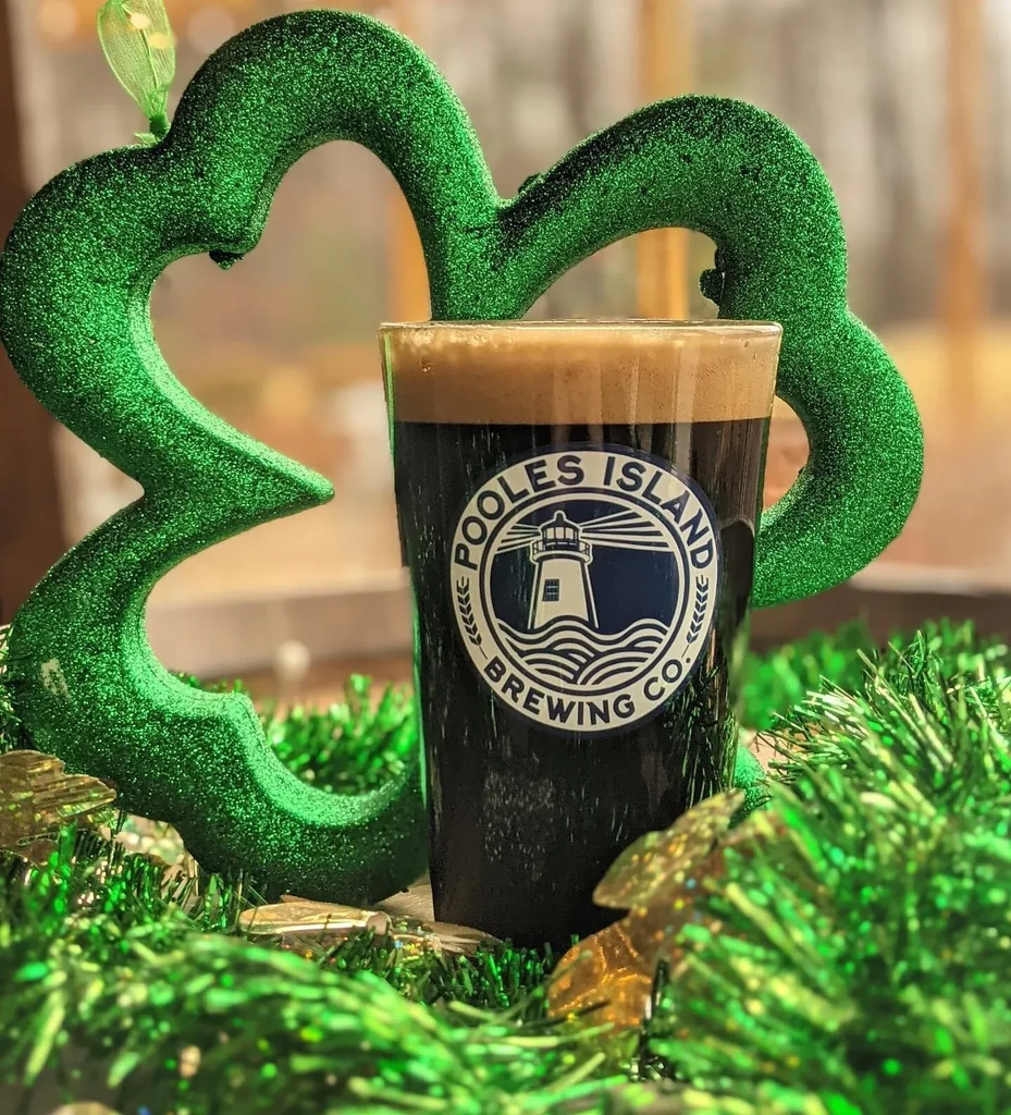Glass of dark beer with Pooles Island logo, framed by green St. Patrick's Day decor.