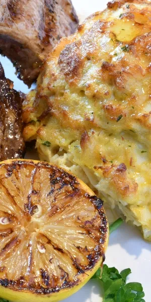Crab cake, grilled meat, grilled lemon, and parsley on a white plate.