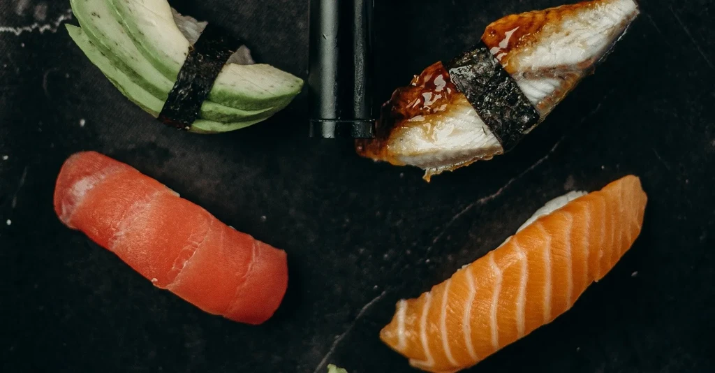 Four nigiri: avocado, eel, tuna, and salmon on dark surface.