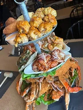 Multi-tiered seafood tower with fried items, shrimp, oysters, and seasoned blue crabs.