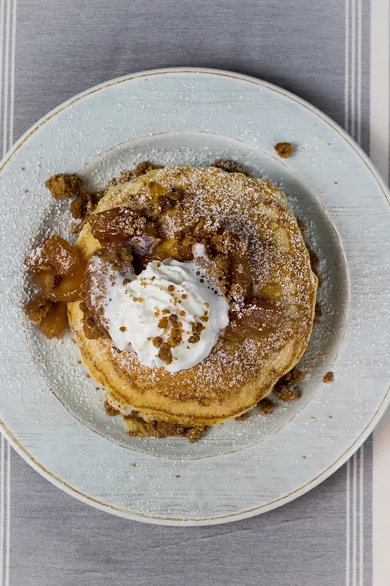 Stack of pancakes topped with whipped cream, crumble and powdered sugar