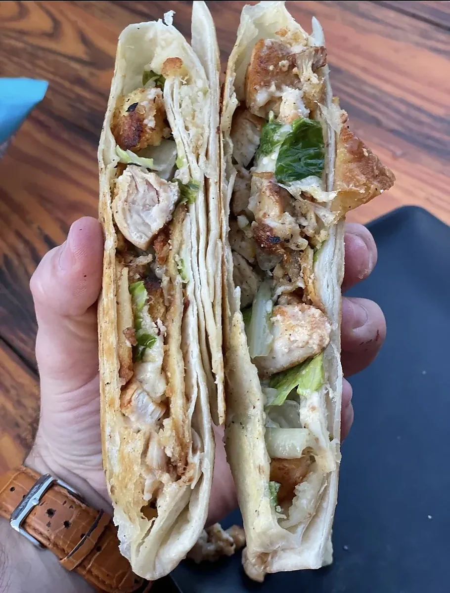 Hand holding halved chicken caesar crunchwrap with lettuce and cheese