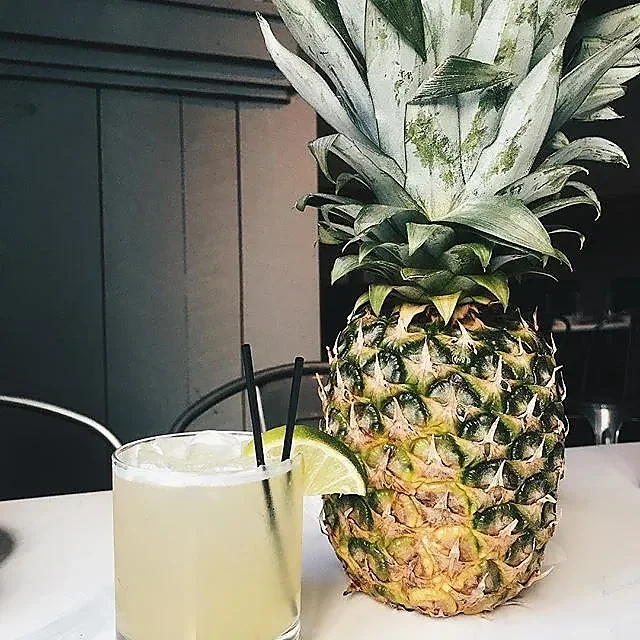 Iced cocktail with lime wedge beside a whole pineapple on table