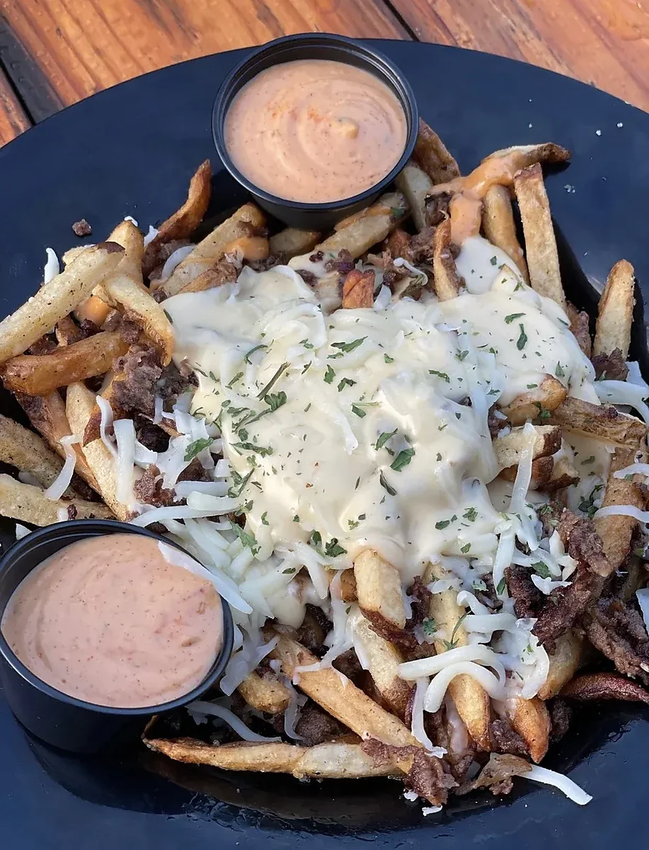 Cheesesteak fries with melted cheese and two cups of dipping sauce