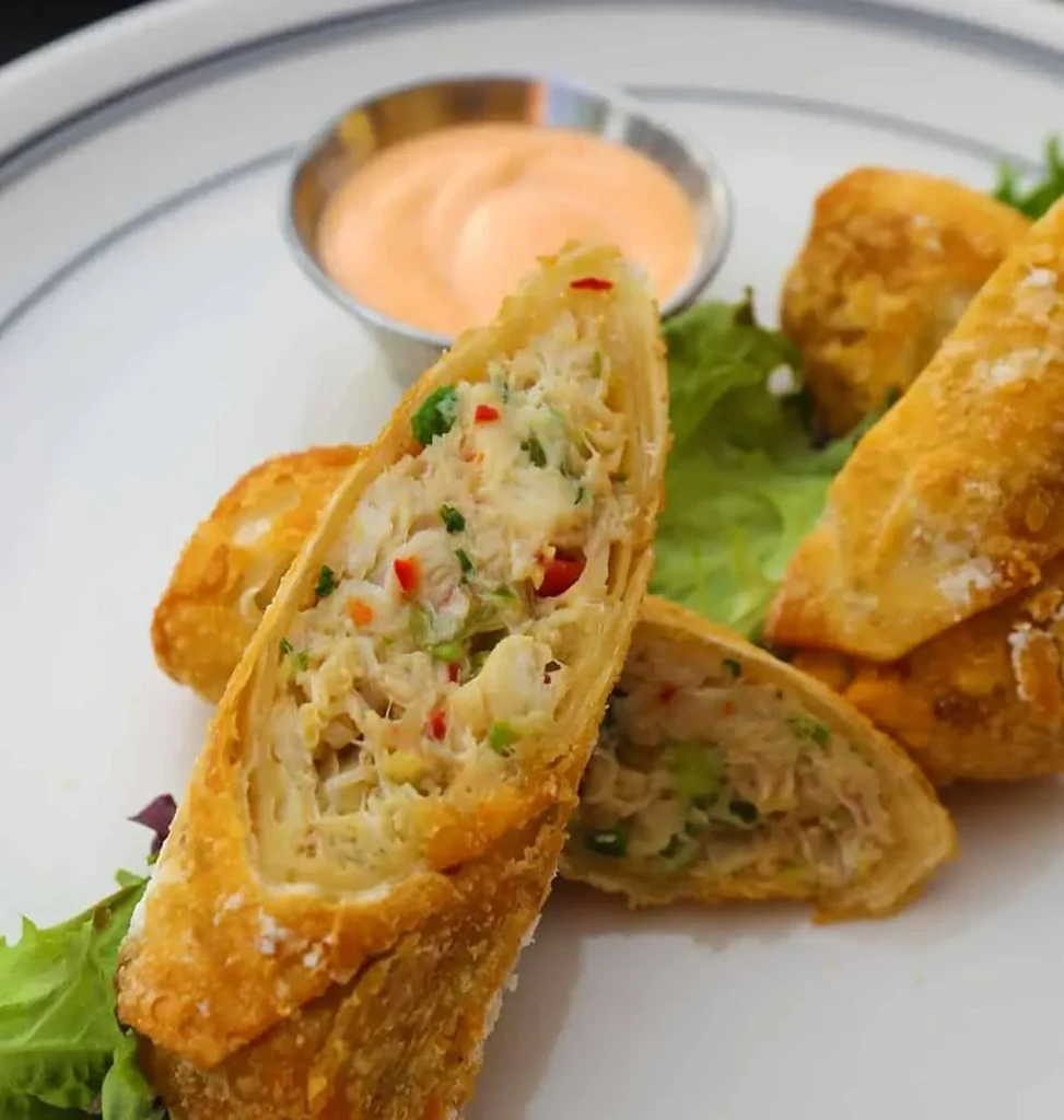 Golden-brown egg rolls with crab and vegetable filling, sauce, and lettuce.