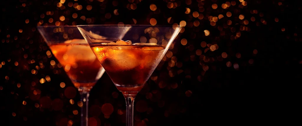 Two martini glasses with amber drinks and ice, warm bokeh background.