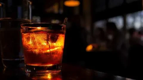 Glowing amber drink with ice on a dark reflective bar top.
