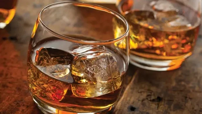 Two whiskey glasses with ice on a textured wooden bar.
