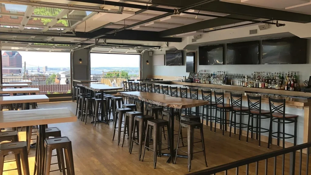 Modern restaurant with bar, mixed seating, city skyline, and industrial ceiling.