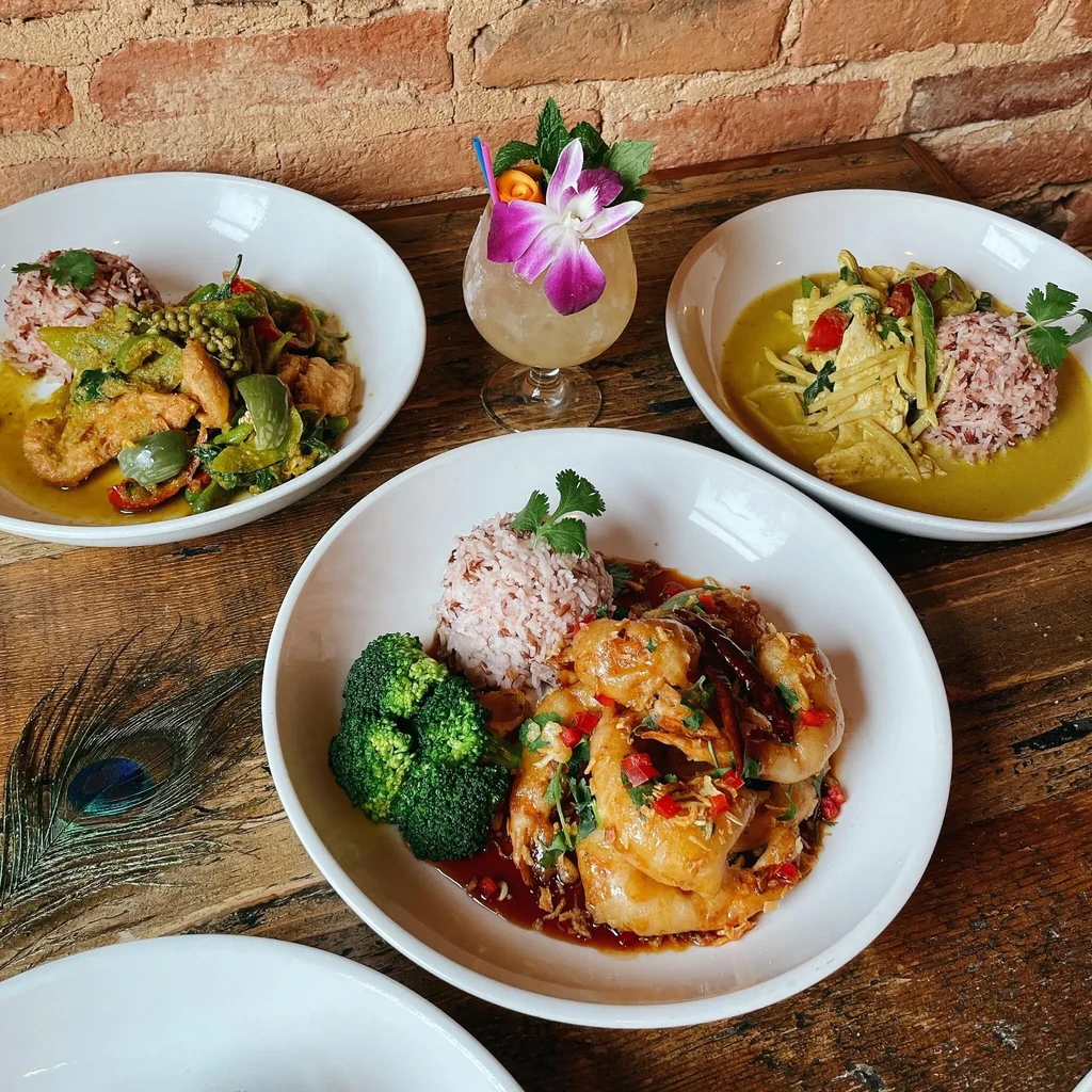 Three Thai curries, shrimp dish, and cocktail on a rustic table.