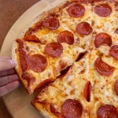 Overhead, a hand lifts a slice from a whole pepperoni pizza.