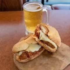 Sub sandwich with melted cheese, red sauce, and cold beer on wood.