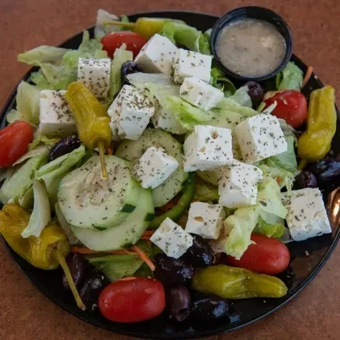 Overhead Greek salad with feta, olives, tomatoes, cucumber, and dressing.