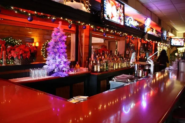 Vibrant Christmas-decorated bar with a long red counter and liquor bottles.